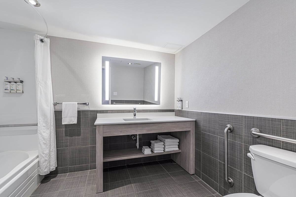 A modern bathroom with a bathtub, a sink with a mirror, a toilet, and a shower curtain.