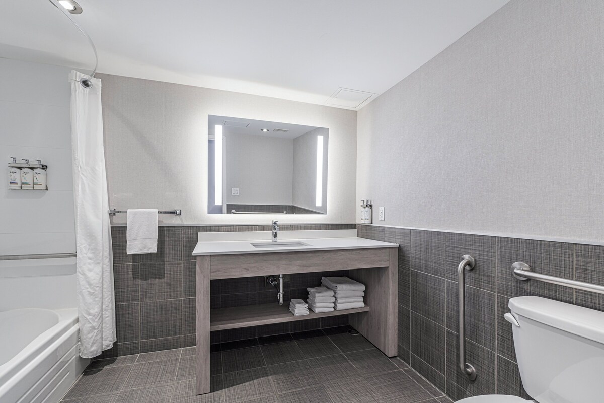 Ein modernes Badezimmer mit Badewanne, Waschbecken mit Spiegel, Toilette und Duschvorhang.