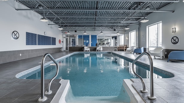 Una piscina interior con barandillas de metal, suelo de baldosas y un techo alto con vigas metálicas.