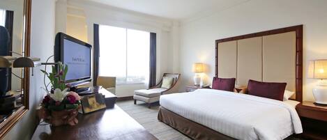 Habitación de hotel con una cama grande, un escritorio con computadora, una silla, televisor y ventana con cortinas.