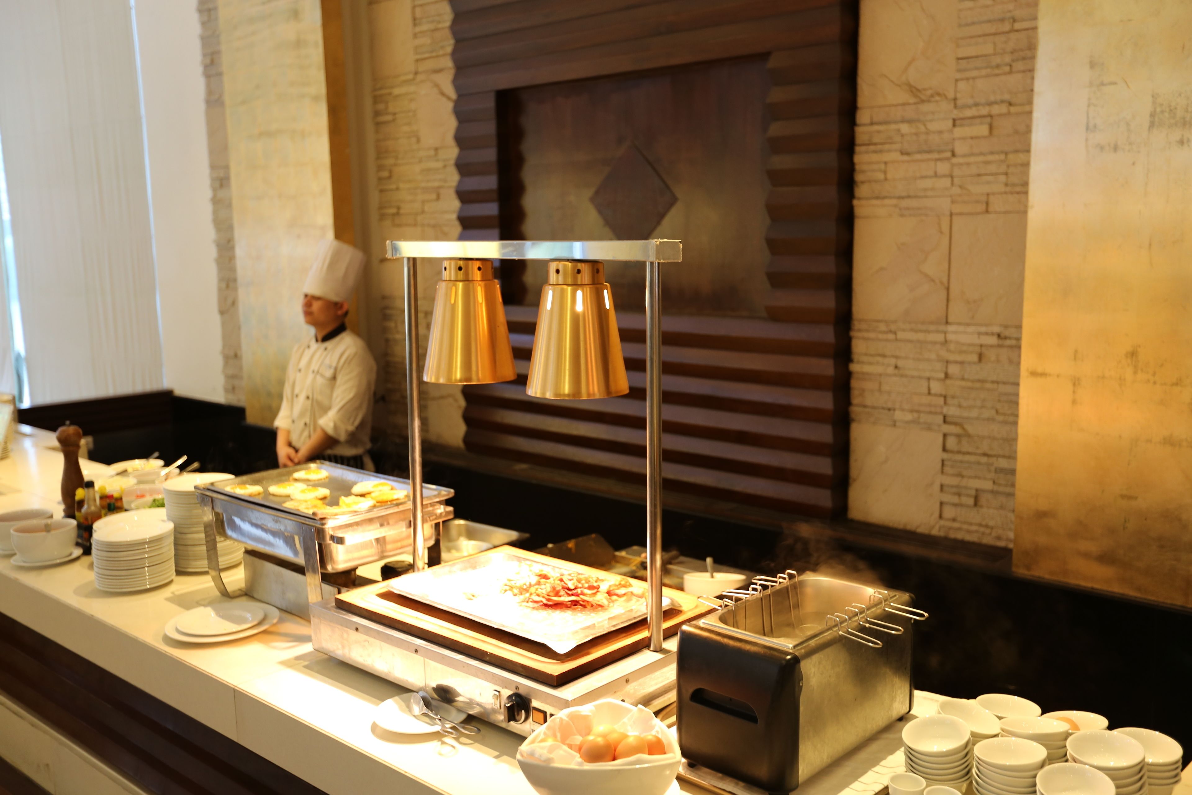 A buffet setup with various food items, a chef, and a modern kitchen backdrop.