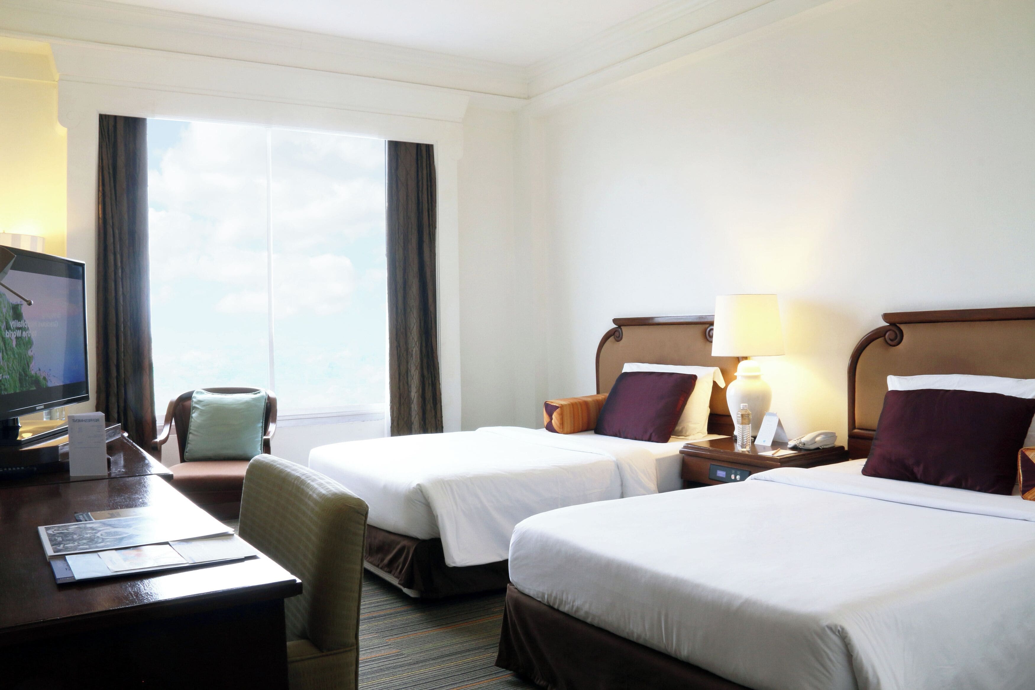 A hotel room with two beds, a desk with a computer, a chair, and a TV.