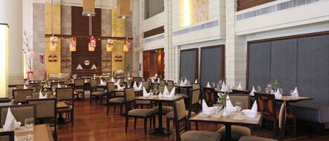 A spacious restaurant with high ceilings, multiple dining tables, and chairs arranged for guests.