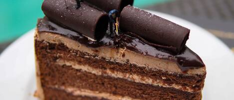 A slice of layered chocolate cake with a glossy chocolate glaze and decorative chocolate pieces on top.