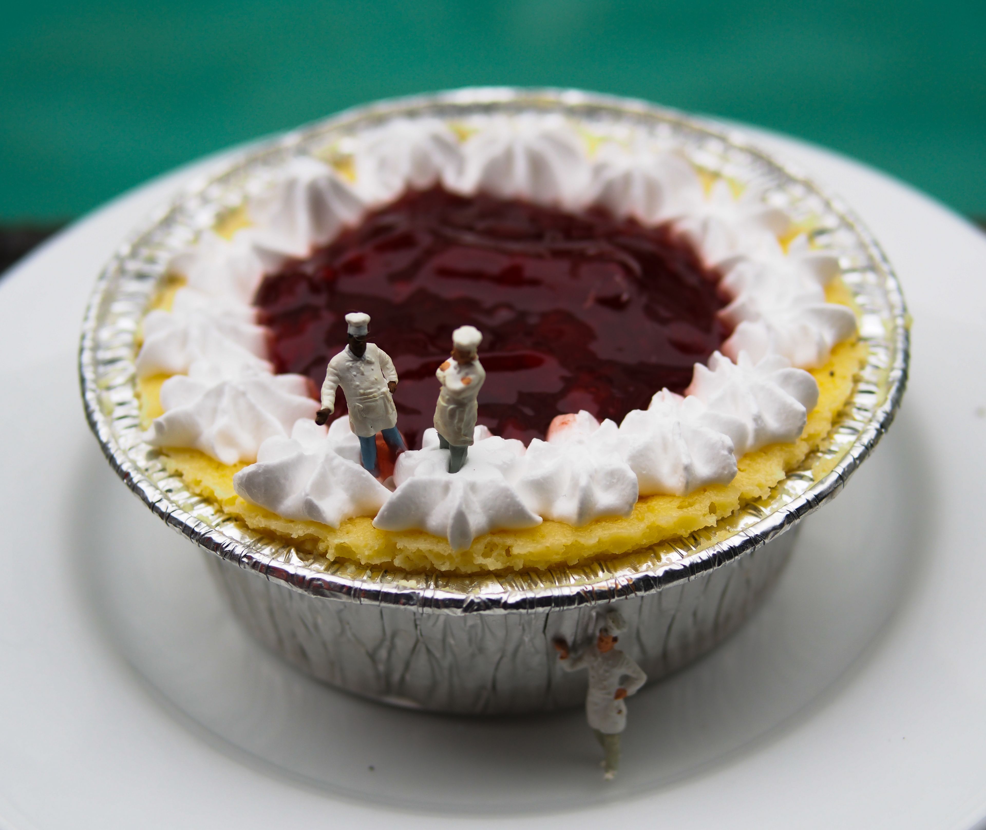 A pie with whipped cream and a cherry filling, served in a foil container.