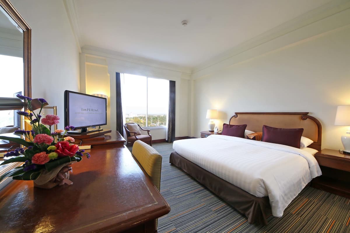 A hotel room with a large bed, a desk with a computer, a chair, a TV, and a window with a view.