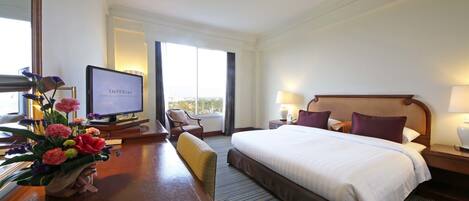 Habitación de hotel con una cama grande, un escritorio con computadora, una silla, un televisor y una ventana con vistas.
