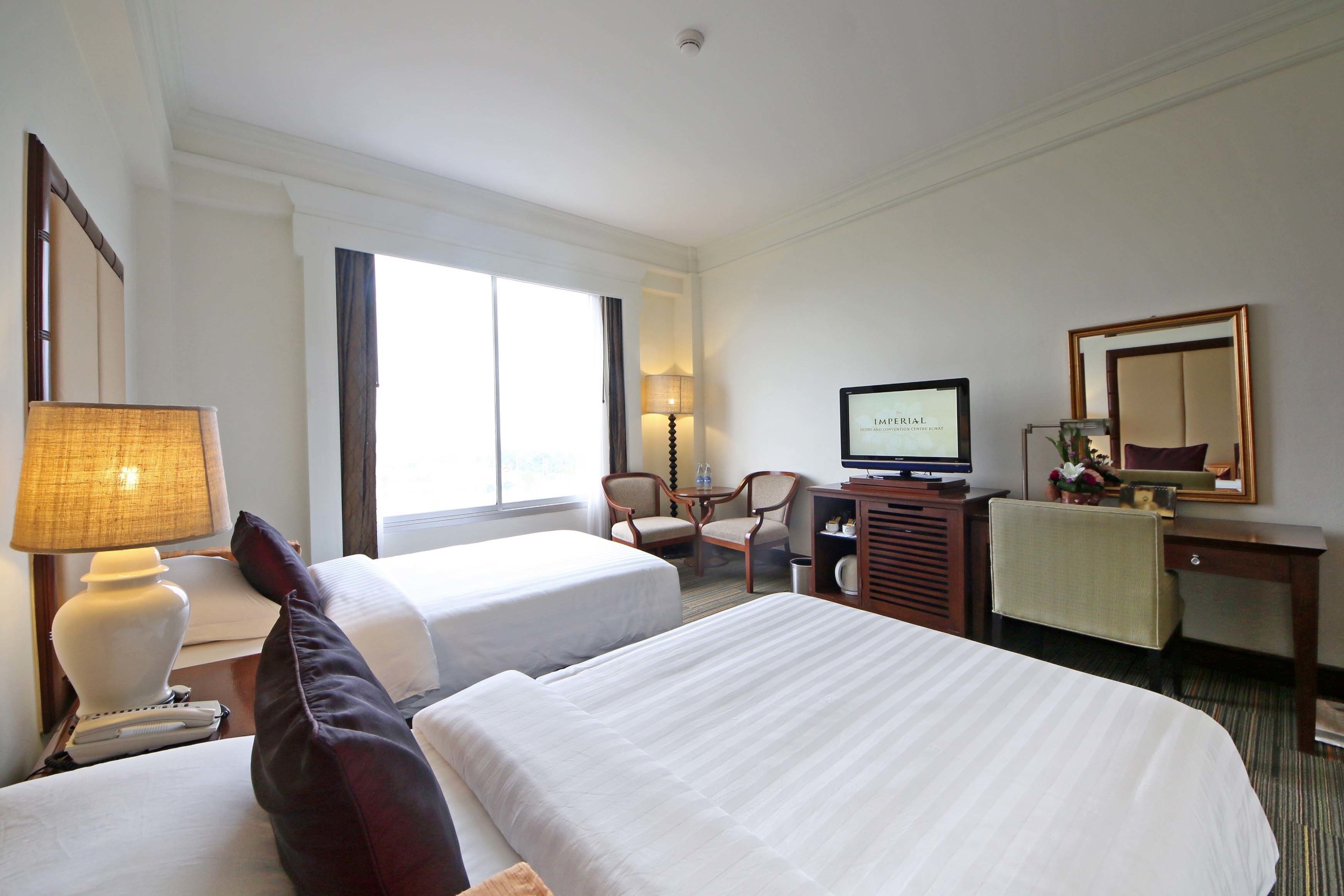 Una habitación de hotel con dos camas, un escritorio con televisor, una lámpara y un espejo.
