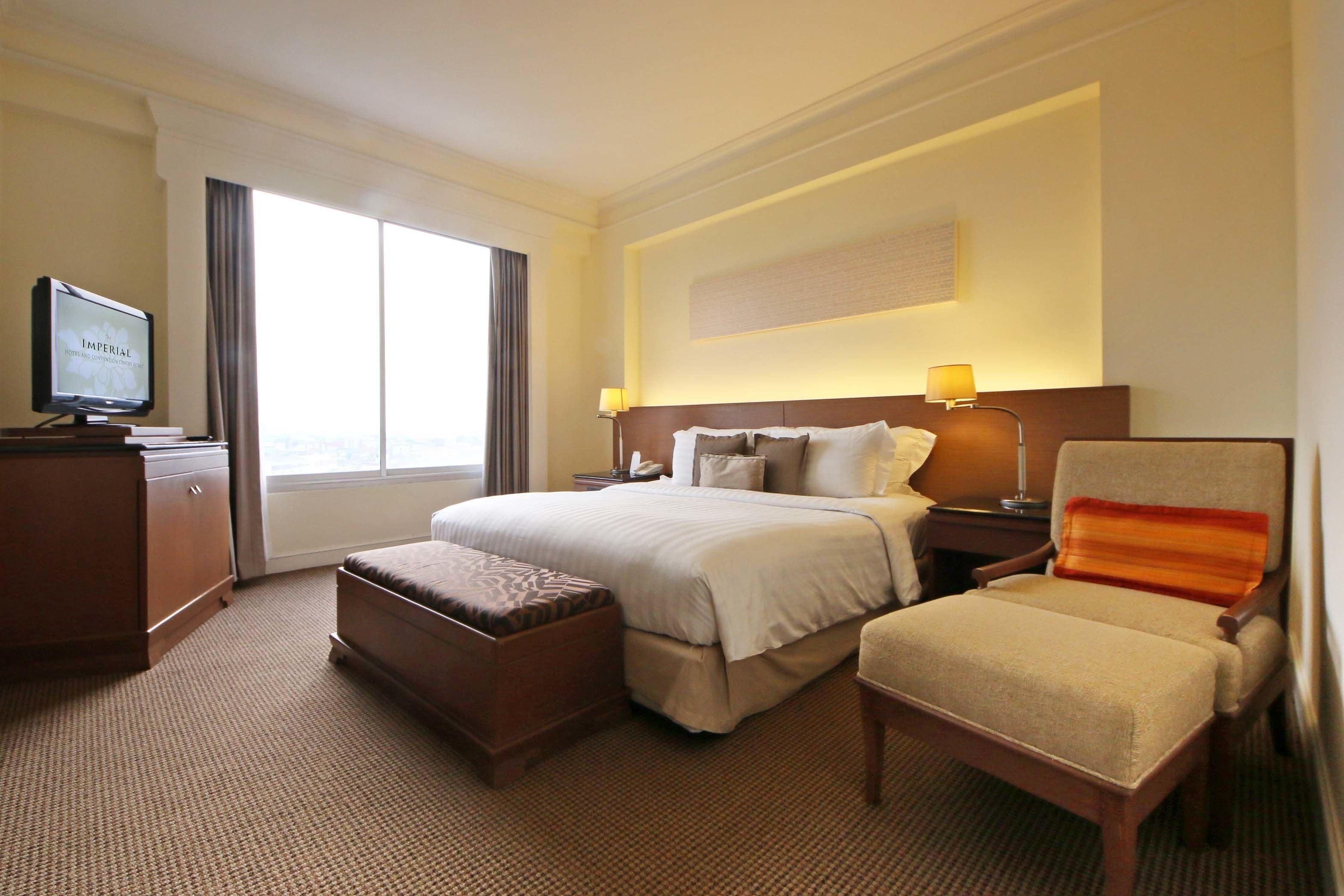 Une chambre d’hôtel avec un grand lit, un bureau avec une télévision, une chaise et une fenêtre avec des rideaux.