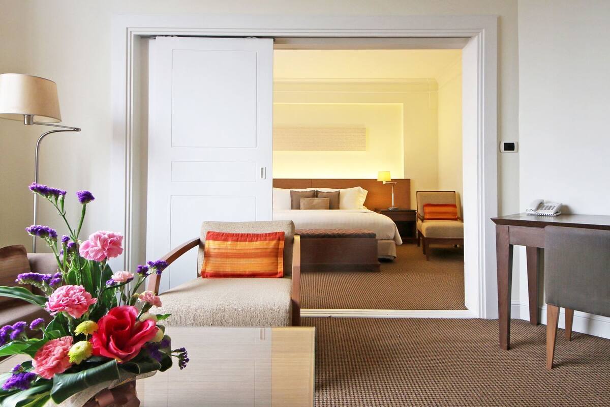 A hotel room with a bed, a desk, a chair, a lamp, and a vase of flowers.