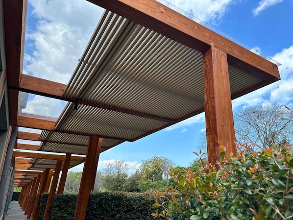 A covered outdoor area with wooden beams and a metal roof, surrounded by greenery. - ibis Styles Catania Acireale (Acireale)