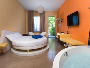 A modern hotel room with a circular bed, a bathtub, a vanity with a mirror, and a television on the wall. - ibis Styles Catania Acireale (Acireale)