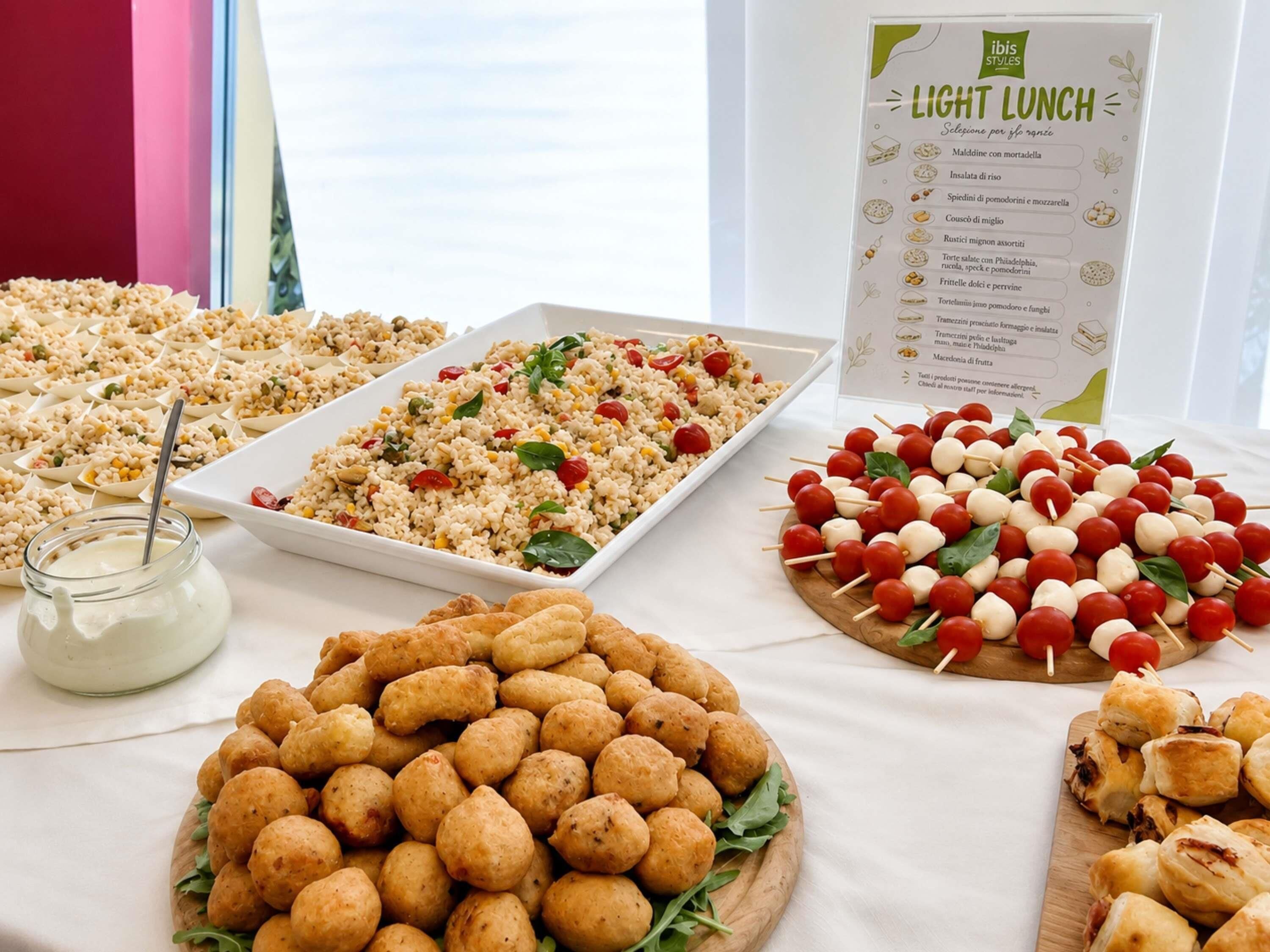Una mesa de buffet con diversos alimentos, como platos de arroz, brochetas de verduras y bollos de pan.