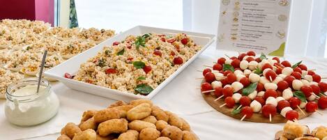 Una mesa de buffet con diversos alimentos, como platos de arroz, brochetas de verduras y bollos de pan.