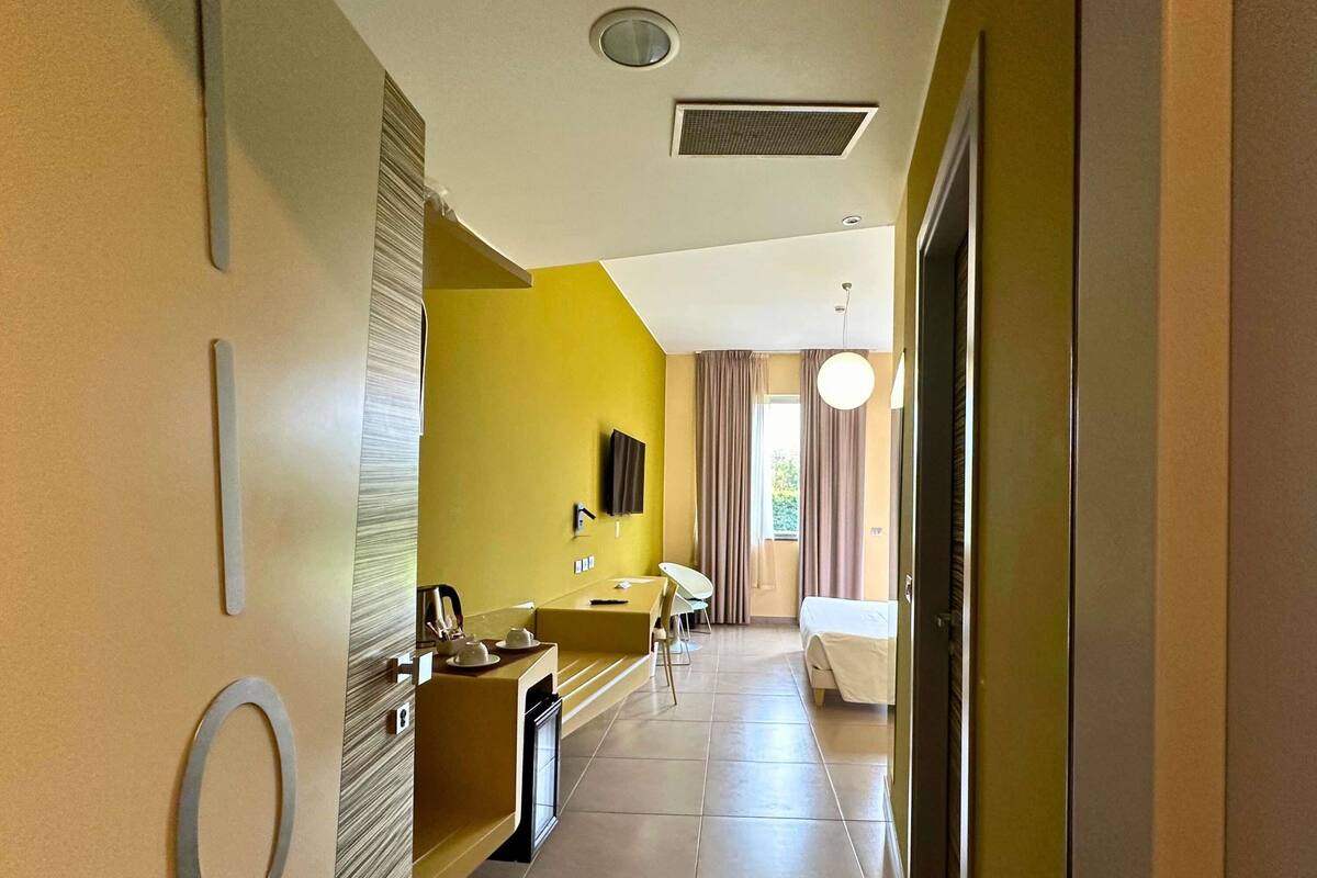 Une chambre d’hôtel avec un lit, un bureau, une chaise, une télévision et une fenêtre avec des rideaux.