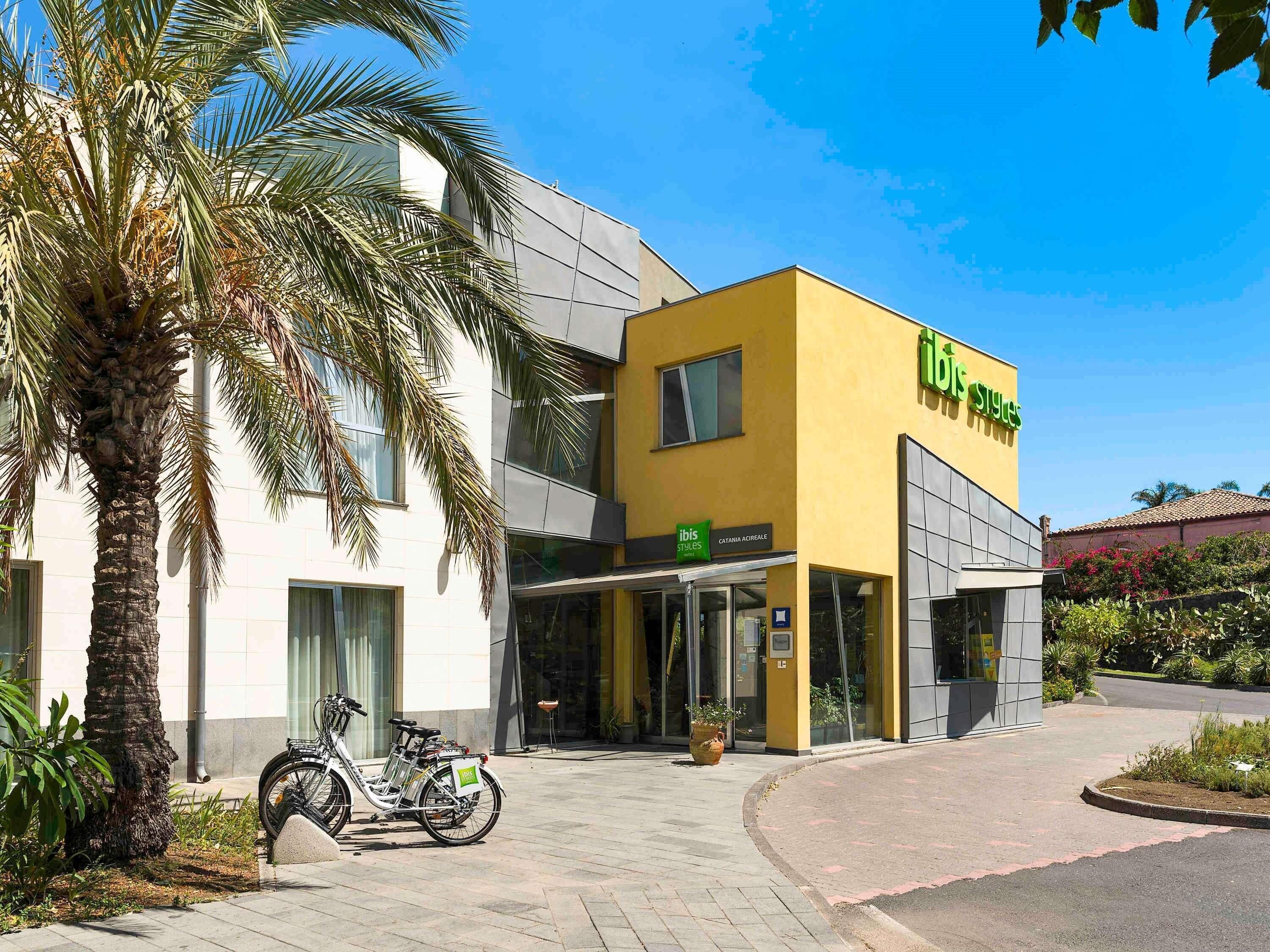 A building with a yellow facade, a sign reading 'ibis styles,' and a parked bicycle.