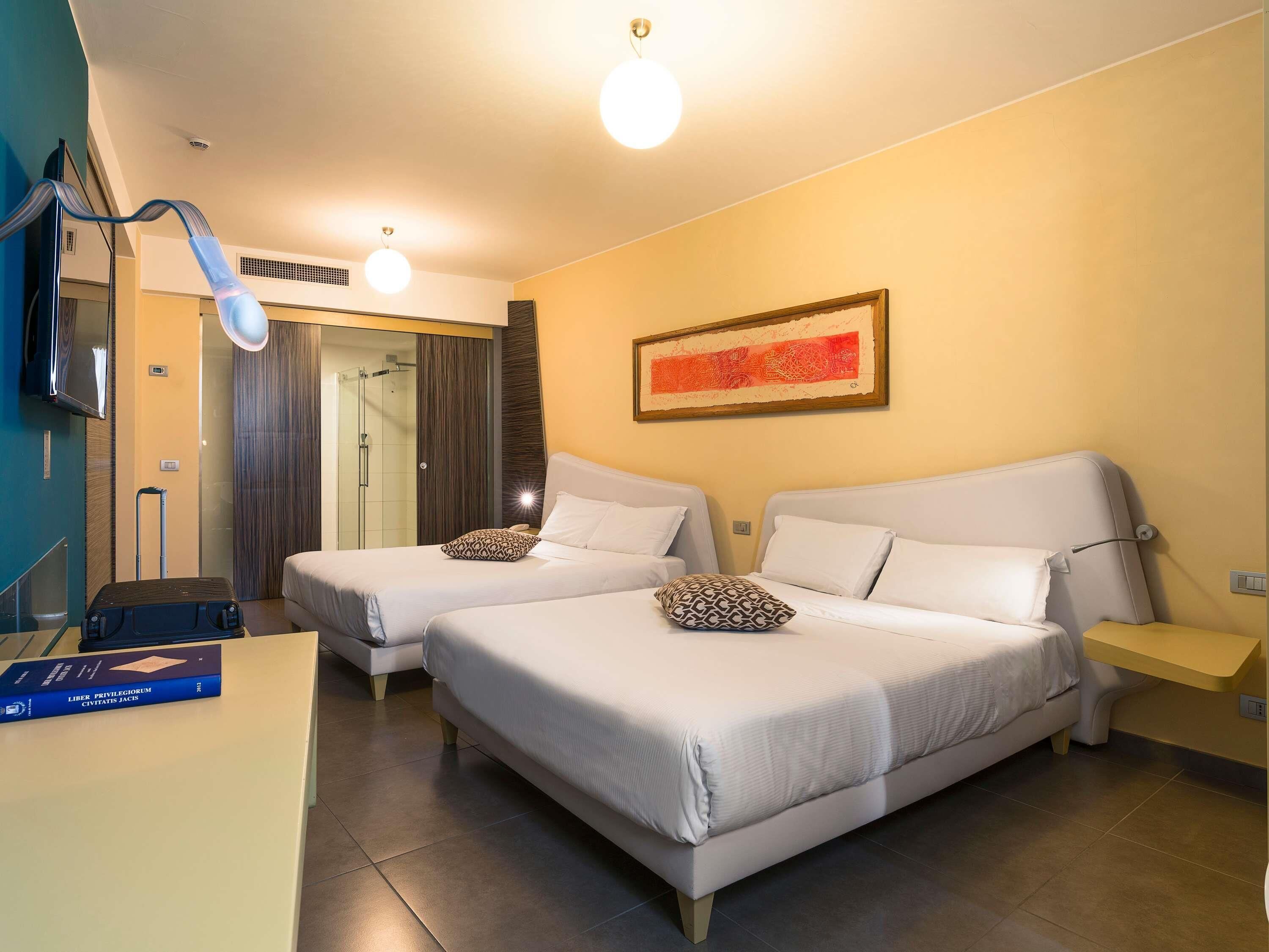 A hotel room with two beds, a desk, a TV, a shower, and a painting on the wall.