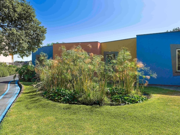 A building with a blue exterior, a grassy area with tall plants, and a clear sky. - ibis Styles Catania Acireale (Acireale)