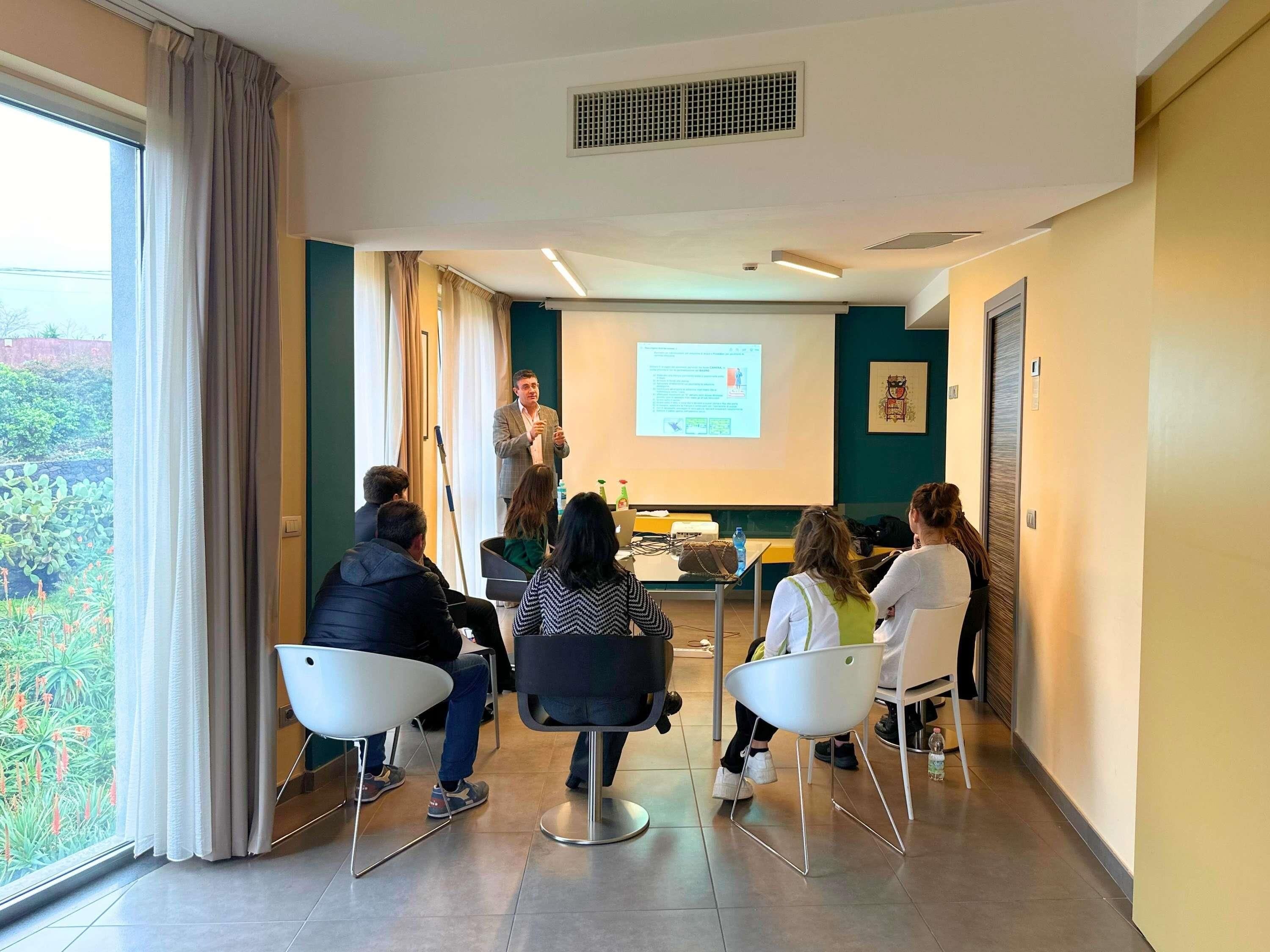 Un salón de conferencias con una pantalla para presentaciones, un proyector y asistentes sentados.