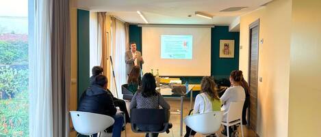 Un salón de conferencias con una pantalla para presentaciones, un proyector y asistentes sentados.