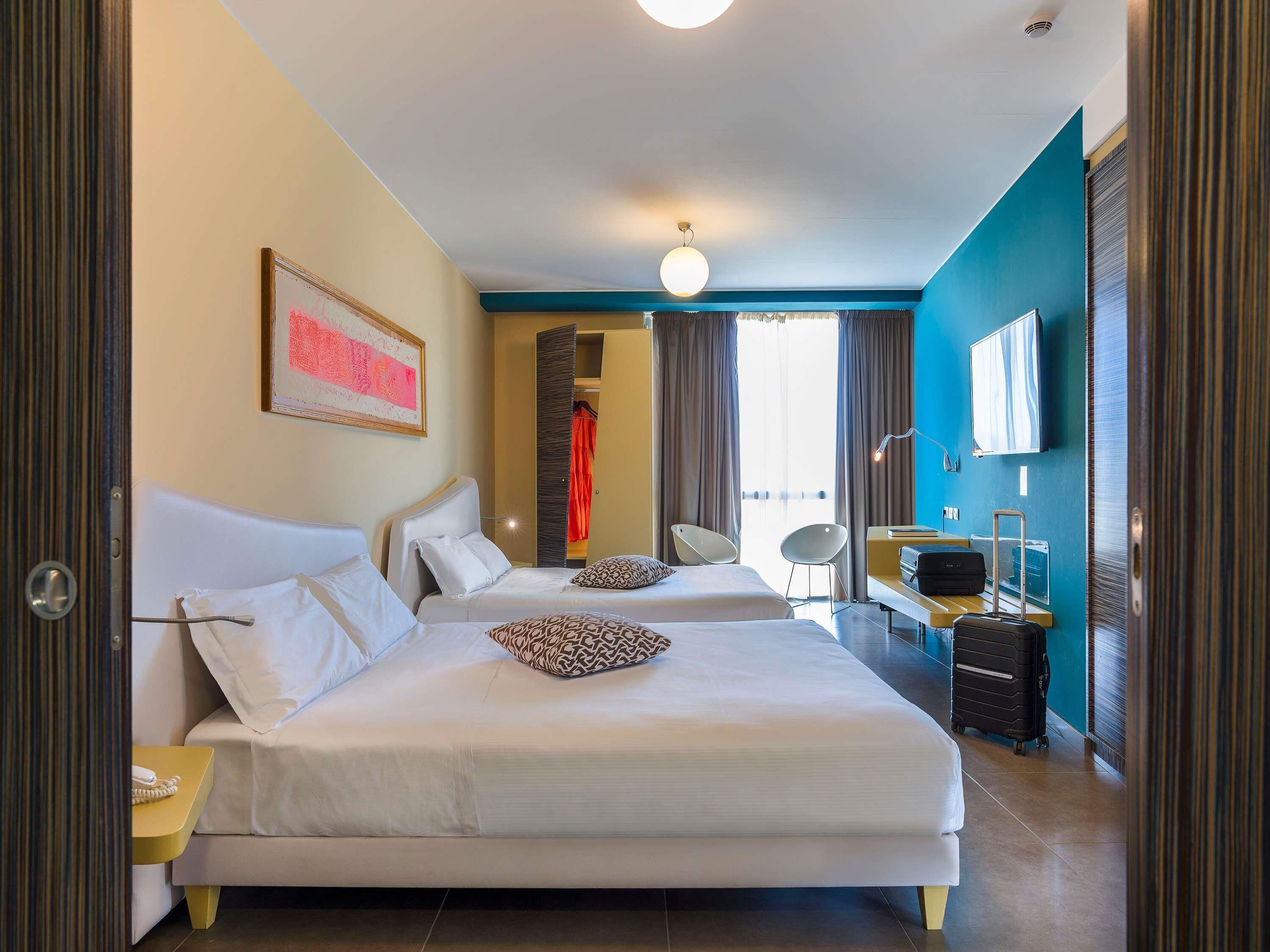 A hotel room with two beds, a desk, a chair, a TV, and a wardrobe.