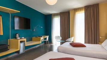 Habitación de hotel con cama, escritorio, silla, televisor y una ventana grande con cortinas.