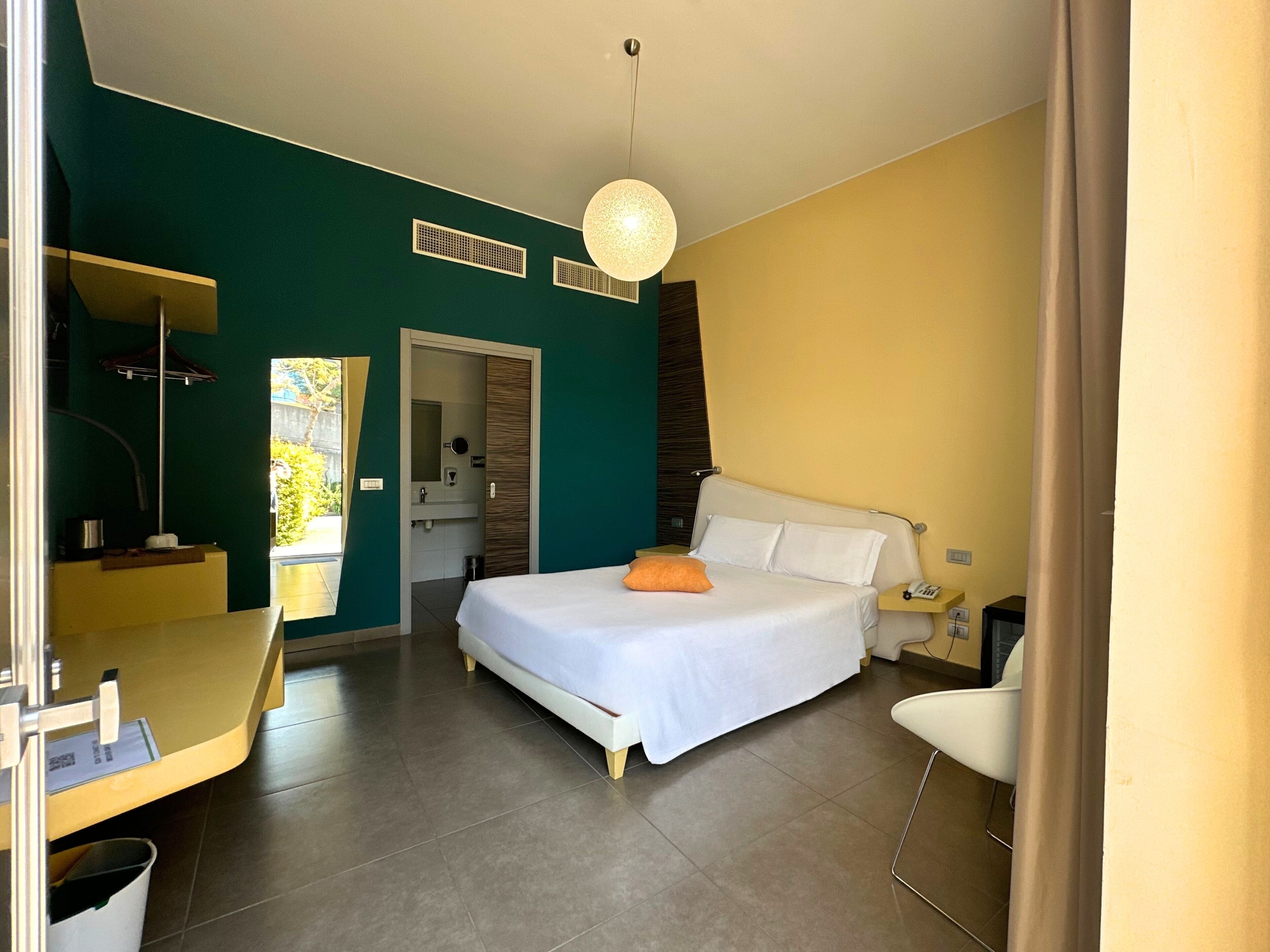 A modern hotel room with a large bed, a desk, and a bathroom visible through an open door.