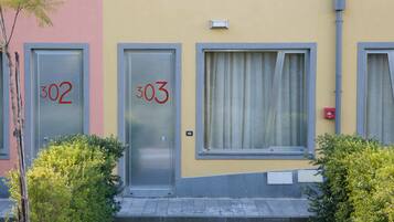 Un edificio con due porte, con le targhette 302 e 303, una finestra con tende e un piccolo spazio verde.