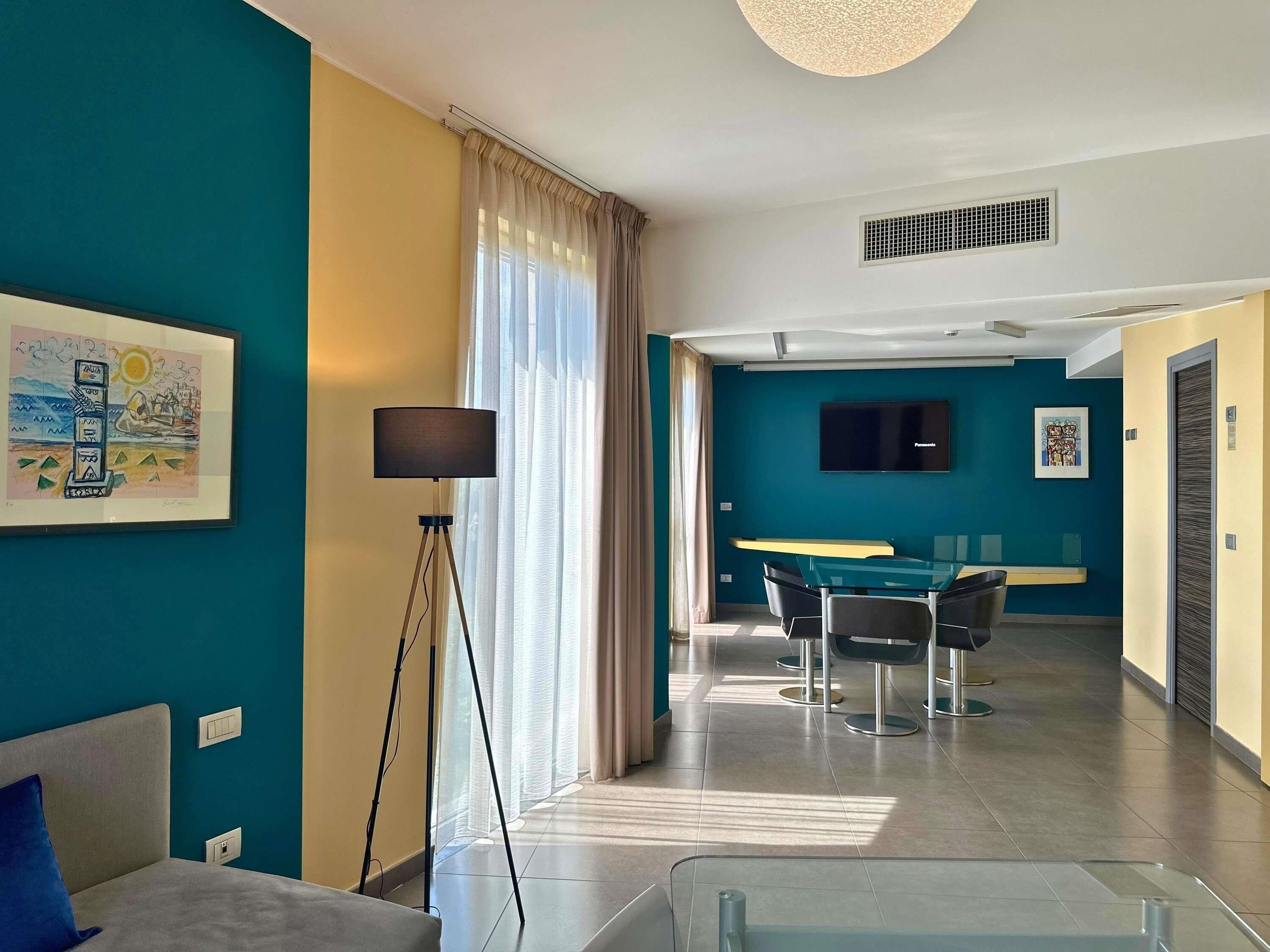 Una habitación de hotel moderna con cama, escritorio, silla, televisor y un ventanal con cortinas.