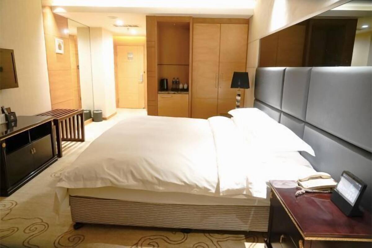 A hotel room with a large bed, a desk with a lamp, a wardrobe, and a television on the wall.