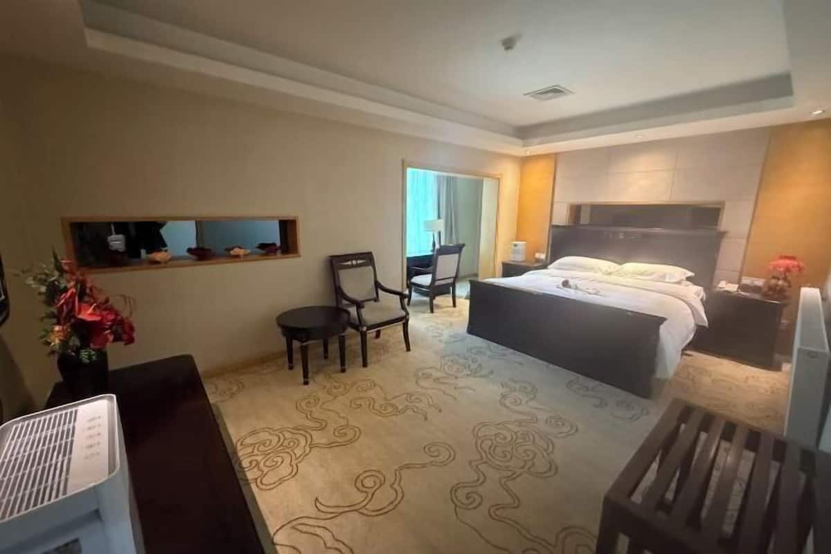 A hotel room with a bed, a desk, a chair, a small table, and a fireplace.
