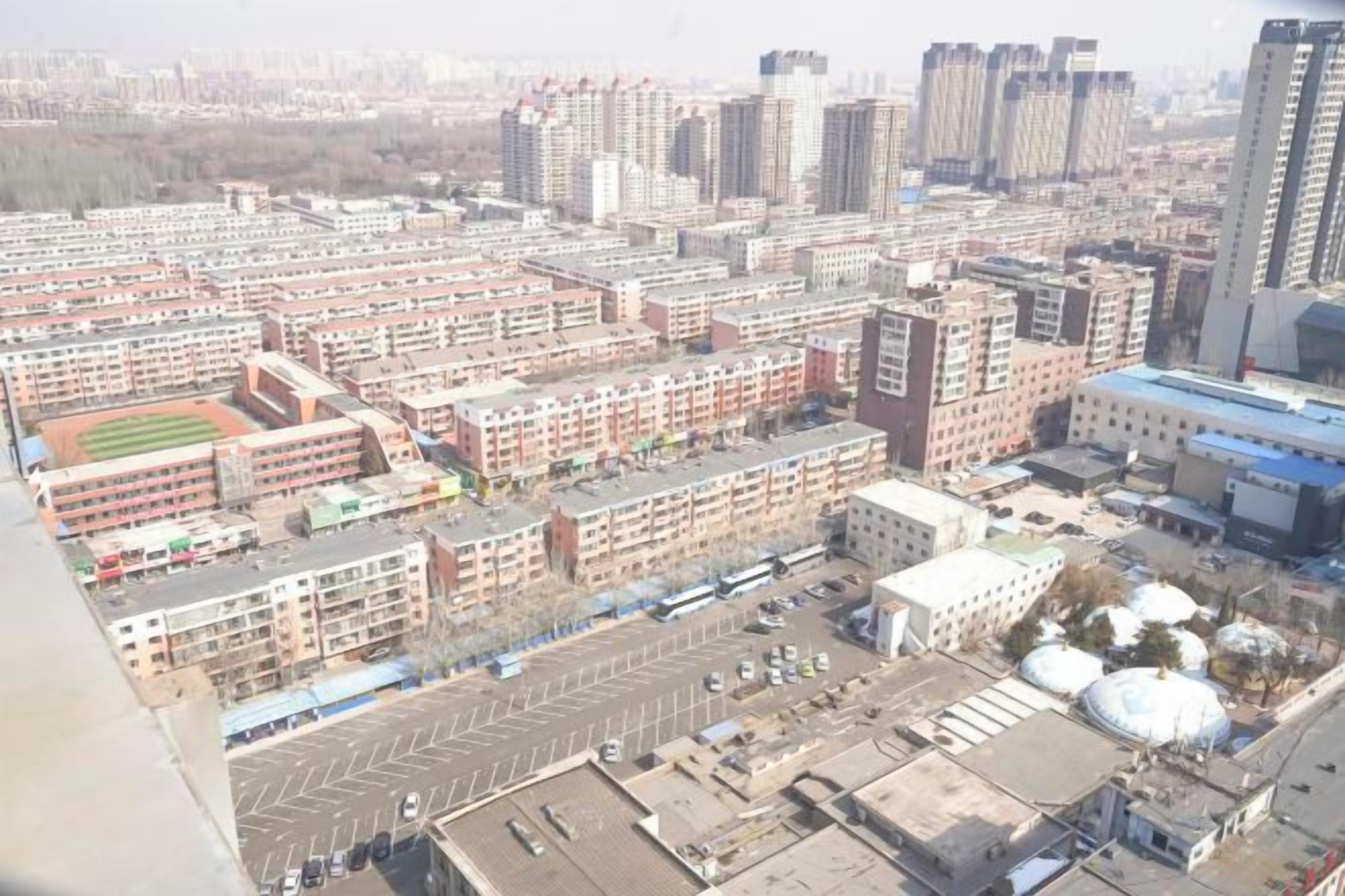 A high-rise building with multiple floors, a parking lot, and a sports field.