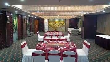 A banquet hall with round tables, white chairs, and a chandelier.