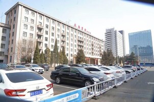 Hotel com vários andares e uma fila de carros estacionados em frente.