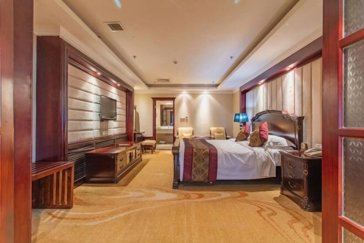 A hotel room with a bed, bedside tables, a TV, and a carpeted floor.