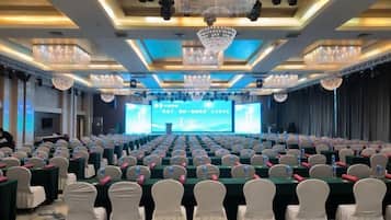 A conference room with rows of tables, chairs, and a stage with a large screen.