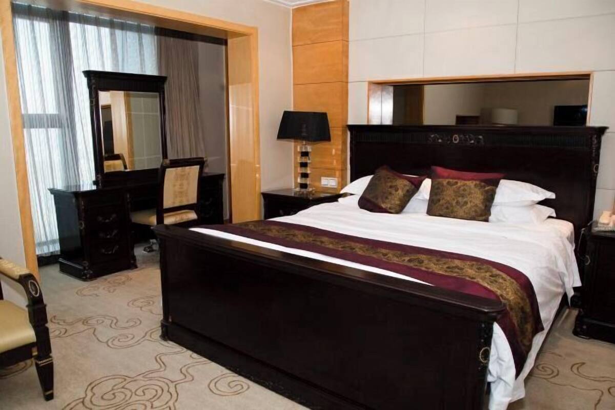 A hotel room with a large bed, a dresser, a mirror, and a nightstand with a lamp.