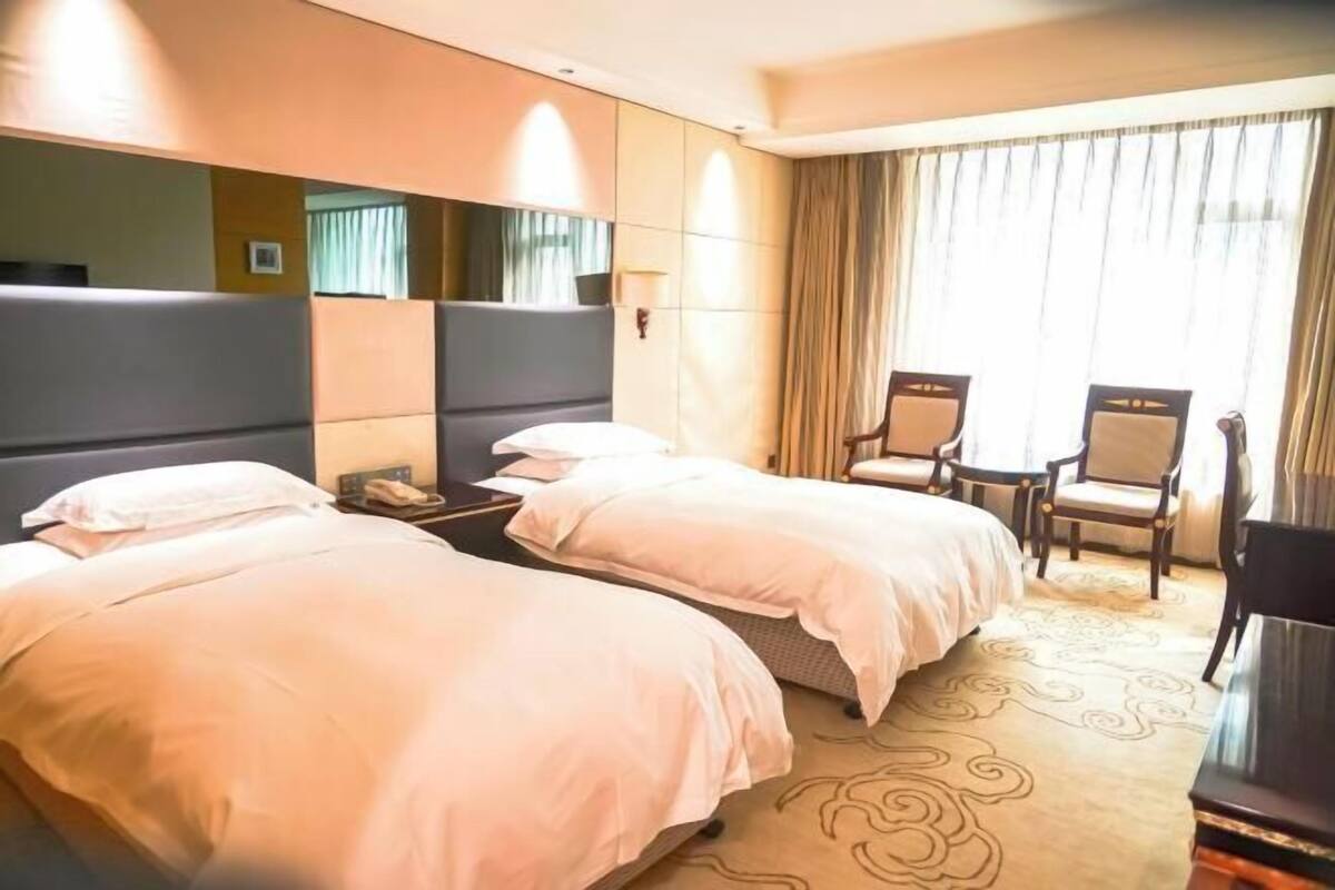 A hotel room with two beds, a desk, a chair, and a large window with curtains.