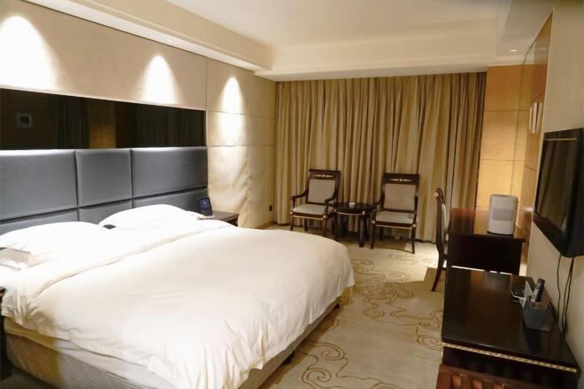 A hotel room with a large bed, a desk, two chairs, a television, and a curtain.