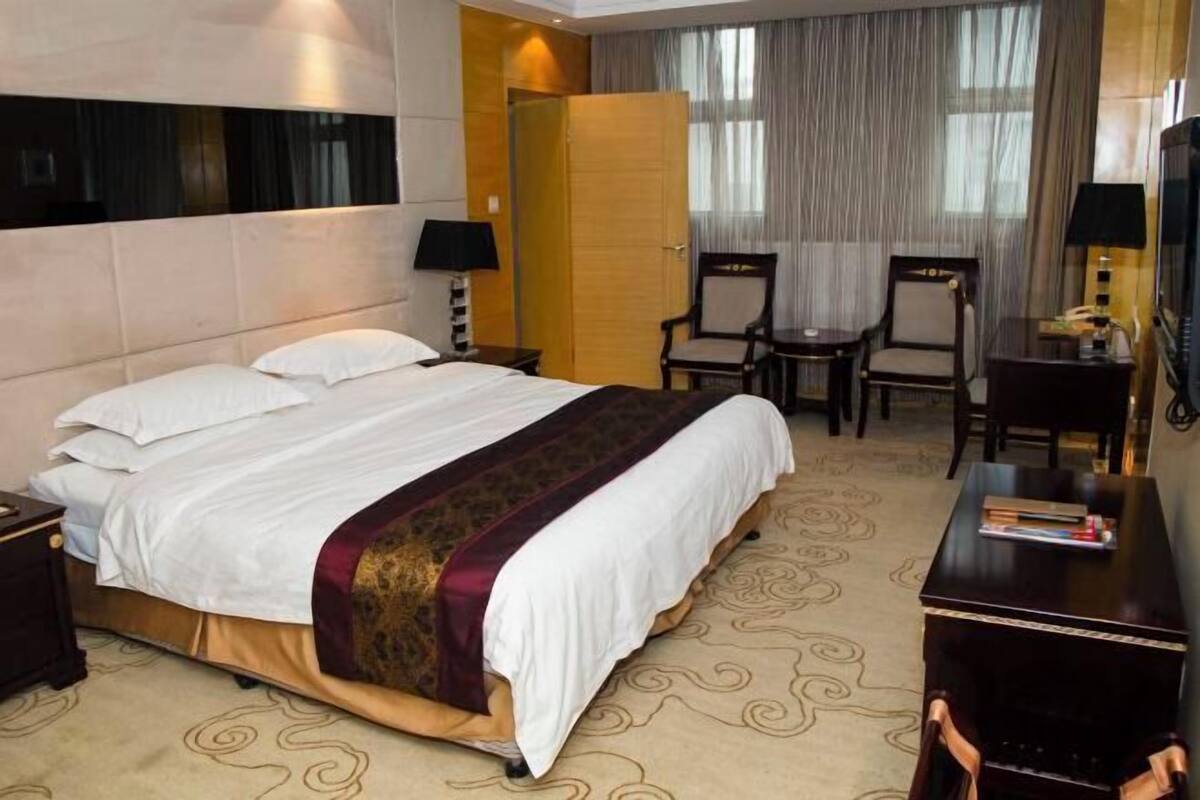 A hotel room with a large bed, two chairs, a desk with a lamp, and a television.