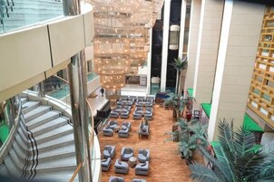 Un vestíbulo de hotel con una escalera central, varias zonas de estar y un techo decorativo.