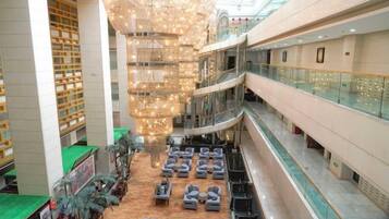 A multi-level hotel lobby with a central chandelier, seating areas, and a glass railing on the upper level.