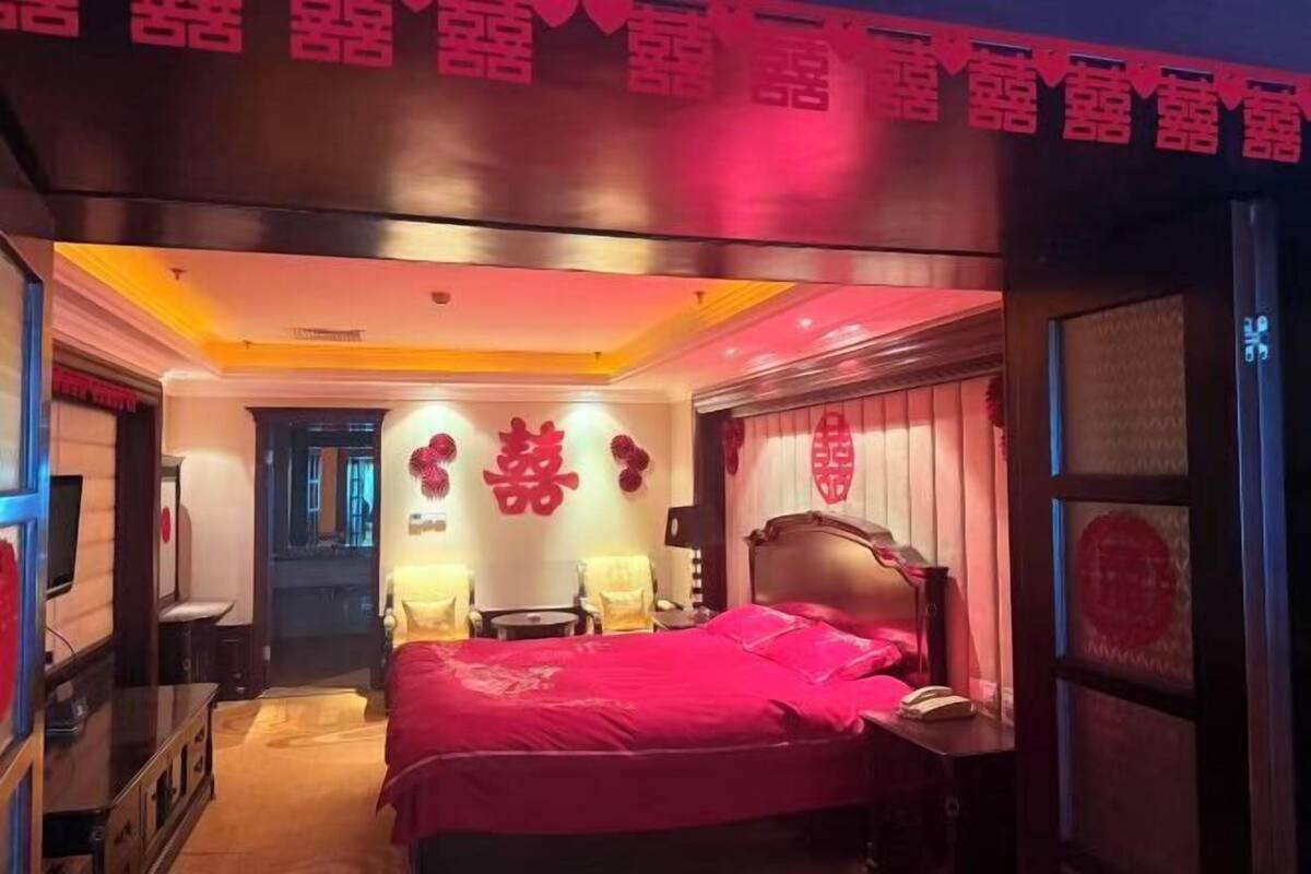A hotel room with a bed, bedside table, and a mirror.