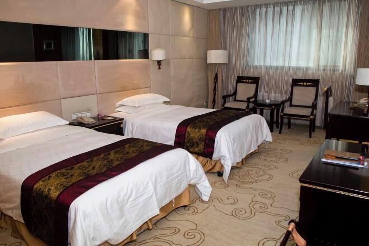 A hotel room with two beds, a desk, chairs, and a large mirror.
