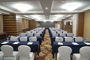 Uma sala de conferências com mesas, cadeiras dispostas em fileiras e piso coberto de carpete.