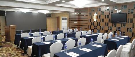 A conference room with rows of tables, white chairs, and a podium.