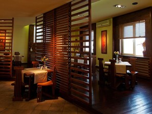 A dining area with wooden partitions, tables, chairs, and a window with blinds. - Hotel Oasis (Brasov)