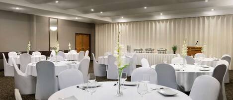 Un salón de conferencias con mesas redondas, sillas blancas y centros de mesa con flores.