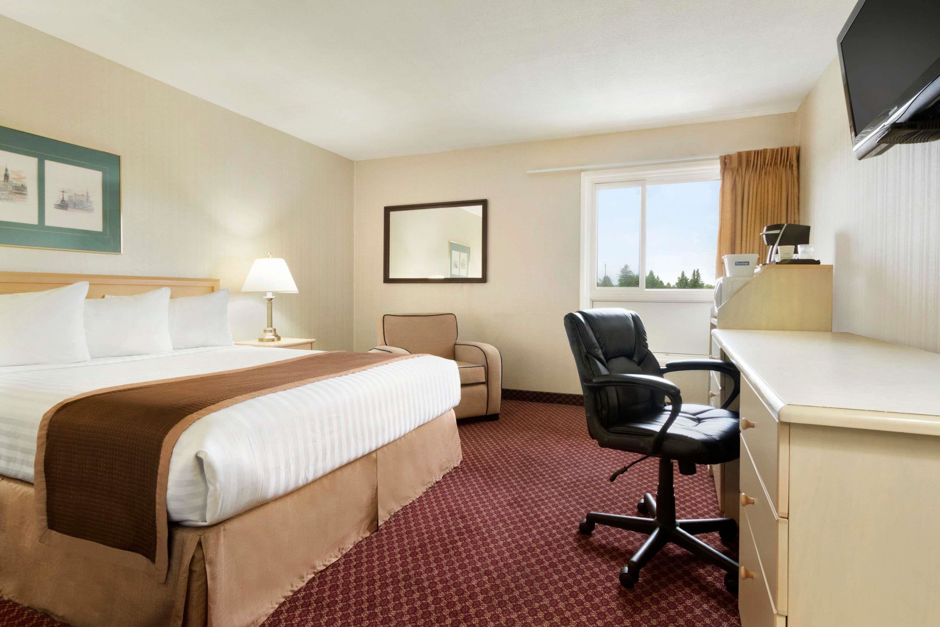 Een hotelkamer met een bed, bureau, stoel, televisie en raam.