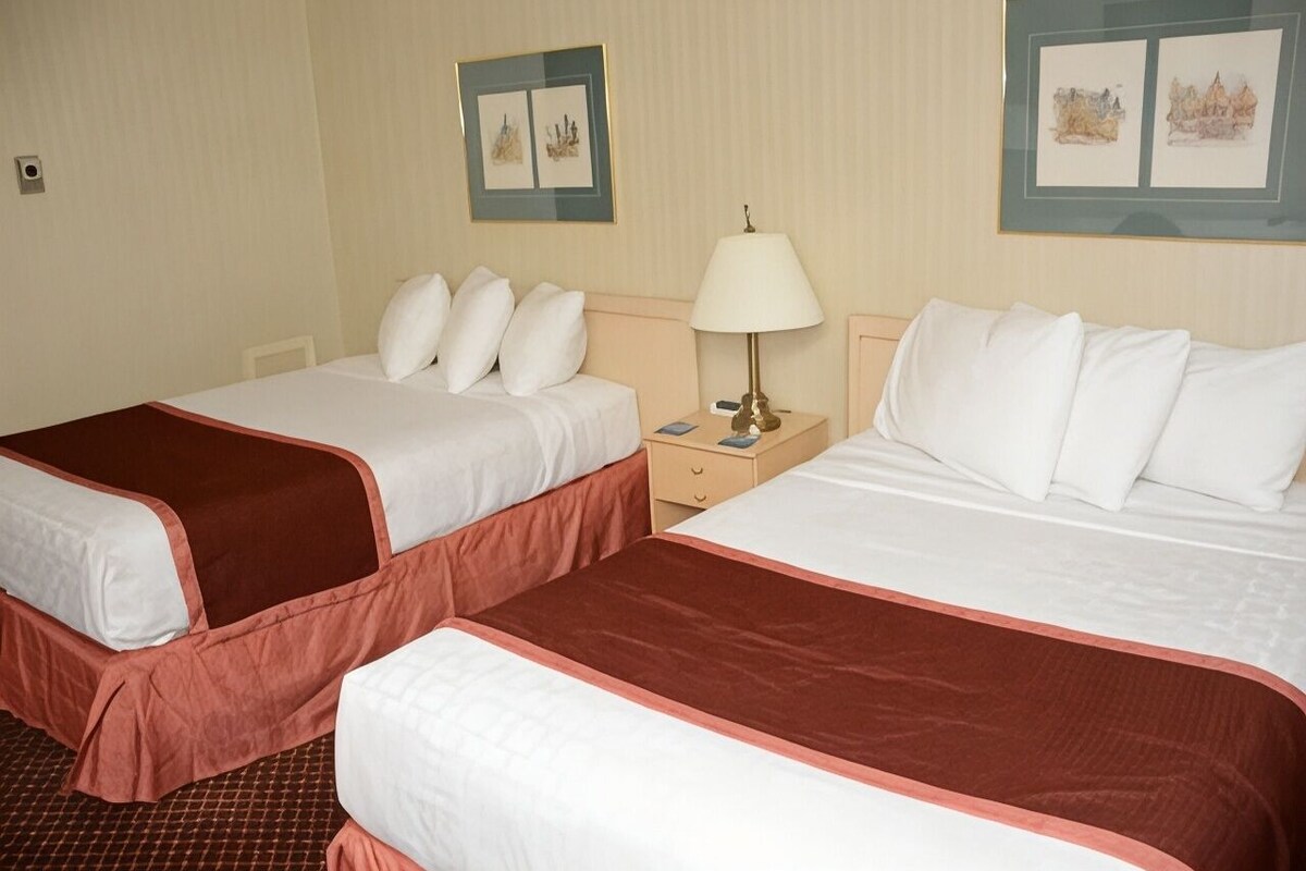 A hotel room with two beds, a nightstand, and artwork on the walls.